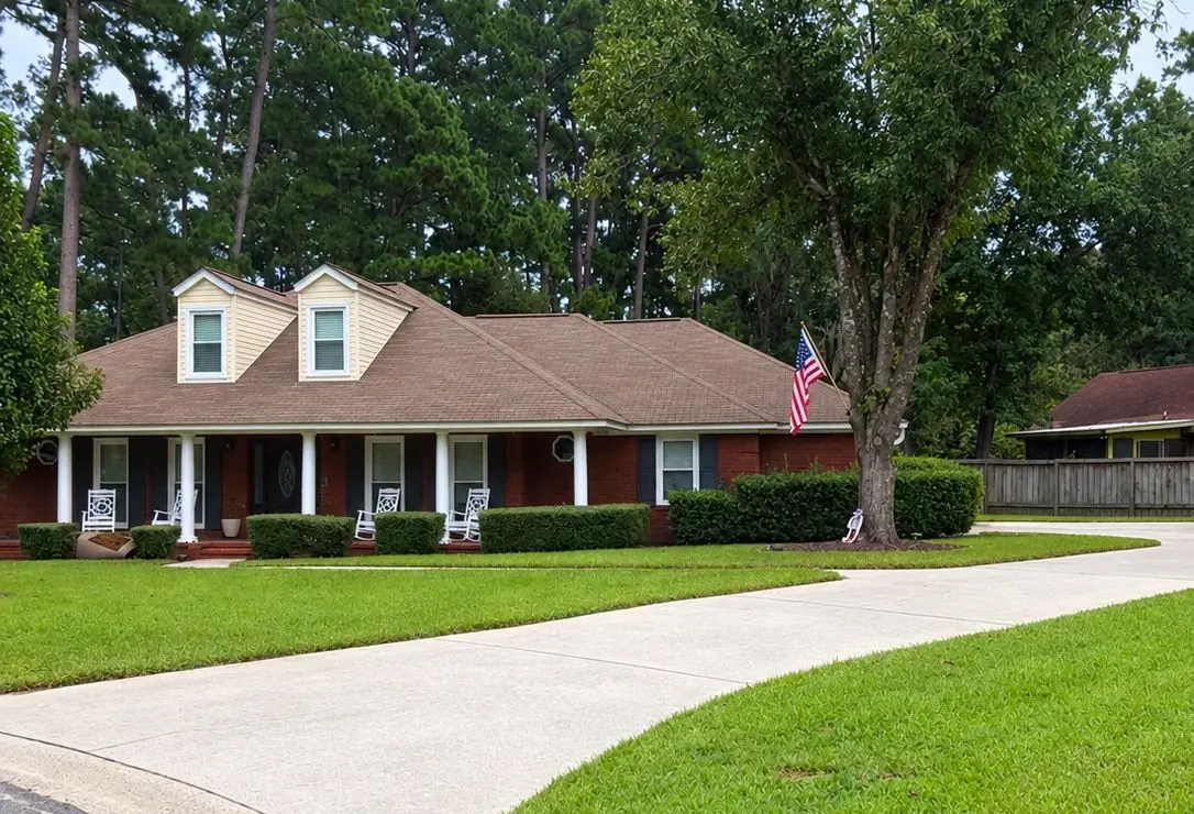 After roof soft washing: the same red brick ranch house with dormers, a front porch and a flag, roof clean